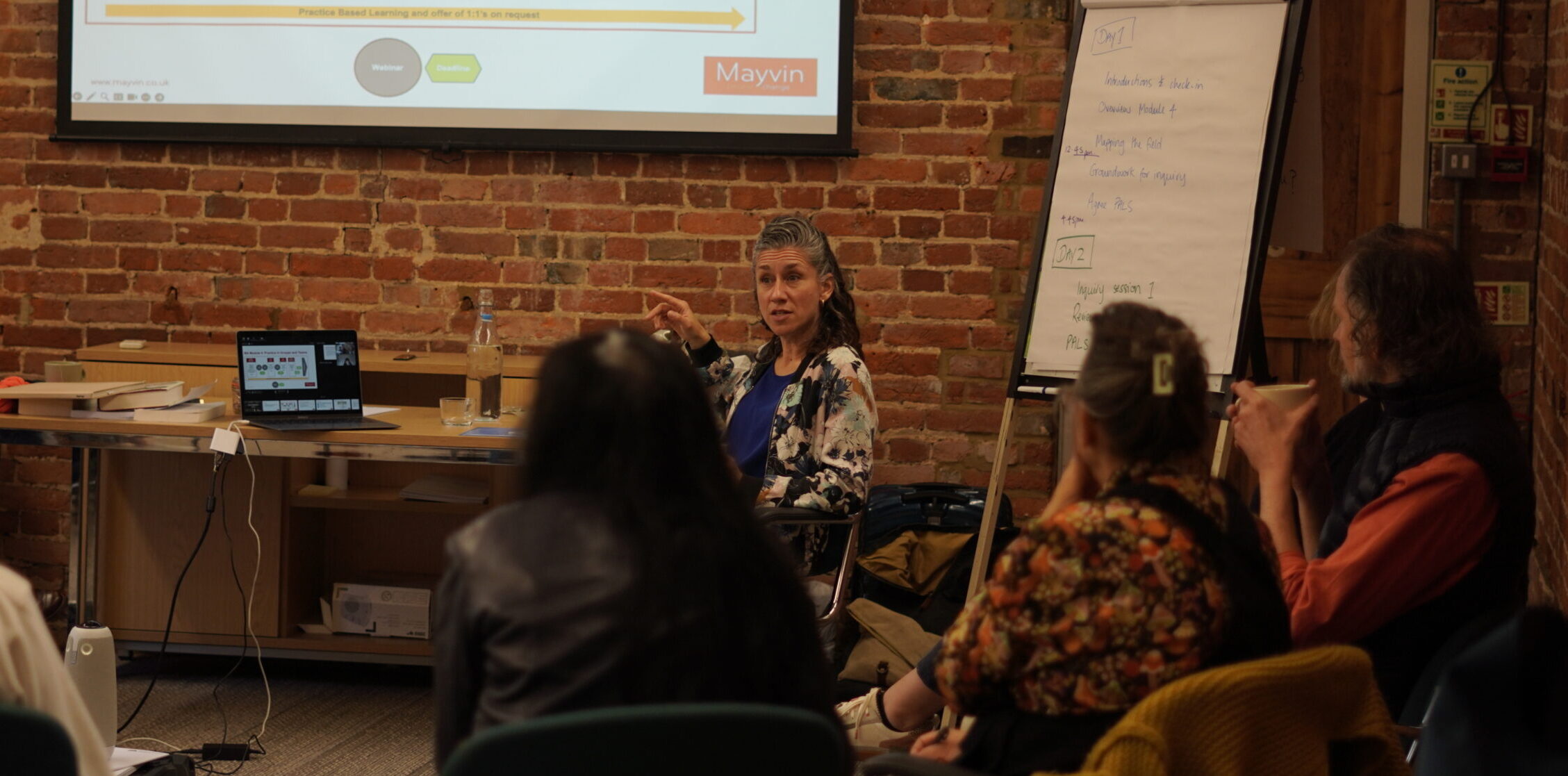 A woman sitting in front of a screen delivering a working session, with a small group watching